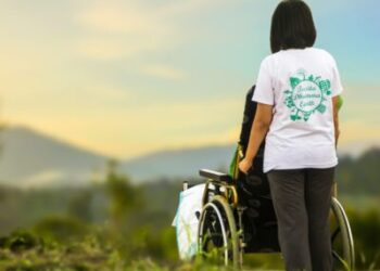 Young woman standing behind an injured person in a wheelchair. They are both looking at nature.