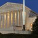 front of supreme court building illuminated against a dark sky
