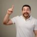 Young man has idea, pointing with finger up isolated on gray background.