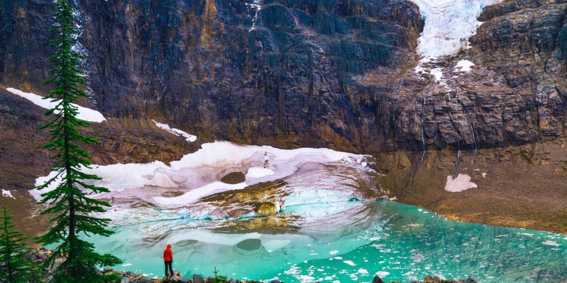 person in red shirt standing on rock near lake