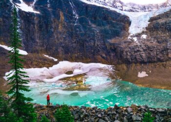 person in red shirt standing on rock near lake