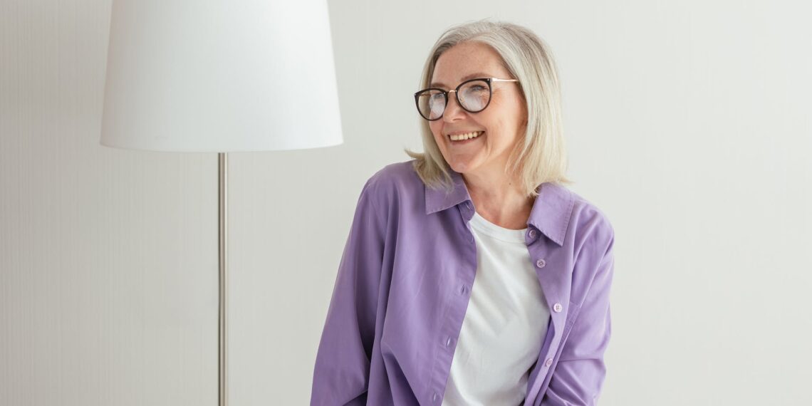 a Canadian senior in purple long sleeves smiling while wearing eyeglasses looking at OAS info
