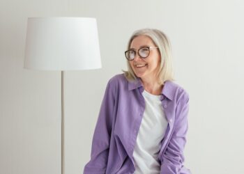 a Canadian senior in purple long sleeves smiling while wearing eyeglasses looking at OAS info