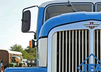 A blue big rig truck from the grill up focused on the large side mirror