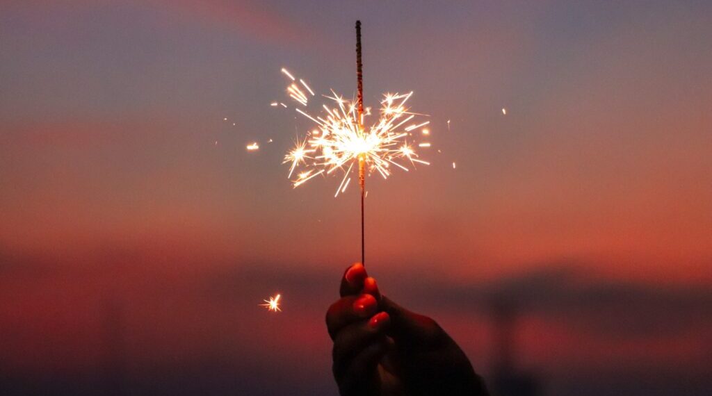 Hand holding a sparkler in front of the sunset.
