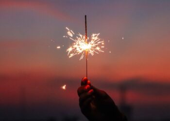Hand holding a sparkler in front of the sunset.