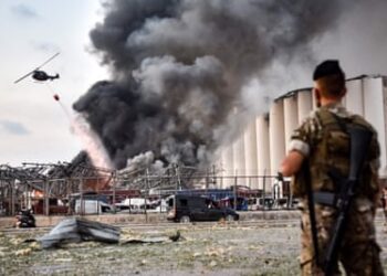 A soldier stands guard as a helicopter extinguishes a fire at the scene of an explosion at Beirut’s port in 2020