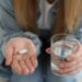 Young woman with abortion pill and glass of water on blurred background, closeup