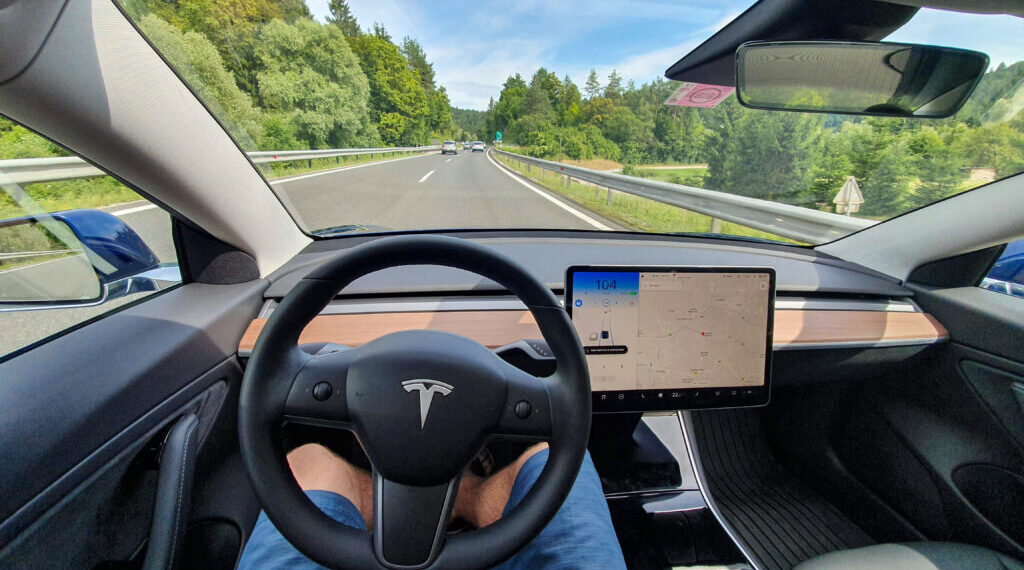 Driving down an empty highway in a high-tech autonomous Tesla vehicle. Young man drives along a scenic rural motorway hands-free in a modern self-steering car.