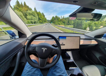 Driving down an empty highway in a high-tech autonomous Tesla vehicle. Young man drives along a scenic rural motorway hands-free in a modern self-steering car.
