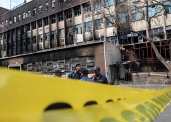 Offers behind a crime scene tape in front of the smoke-blackened building