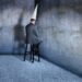 Bunsinessman in dunce cap sits on a stool in corner