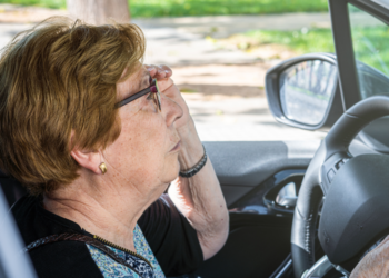 Older woman behind the wheel adjusting her glasses.