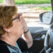 Older woman behind the wheel adjusting her glasses.
