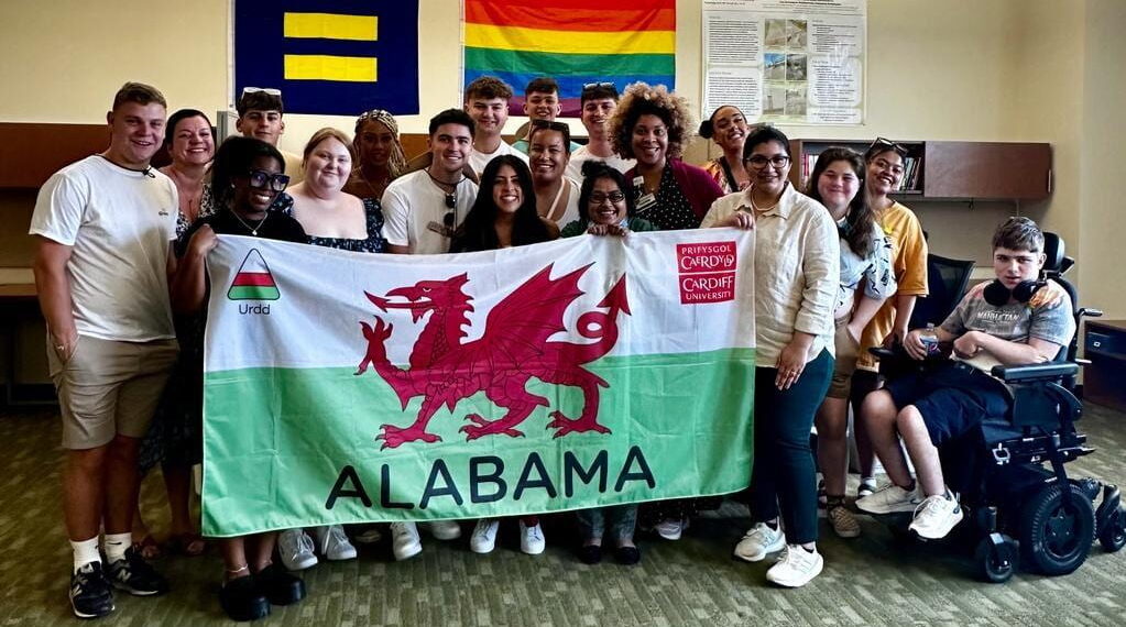 Image shows the Urdd delegation and the IHR team posing with a flag of Wales.