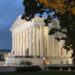 side view of supreme court building, illuminated against dark sky at dusk, with large tree in foreground