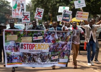 A group of young Africans dressed casually and holding signs above their heads and a banner that says #StopEacop march on what appears to be a sunlit brown road.