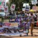 A group of young Africans dressed casually and holding signs above their heads and a banner that says #StopEacop march on what appears to be a sunlit brown road.
