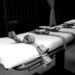 A black and white picture of a prison cot with five belts used to strap down inmates in order to give them a lethal injection.