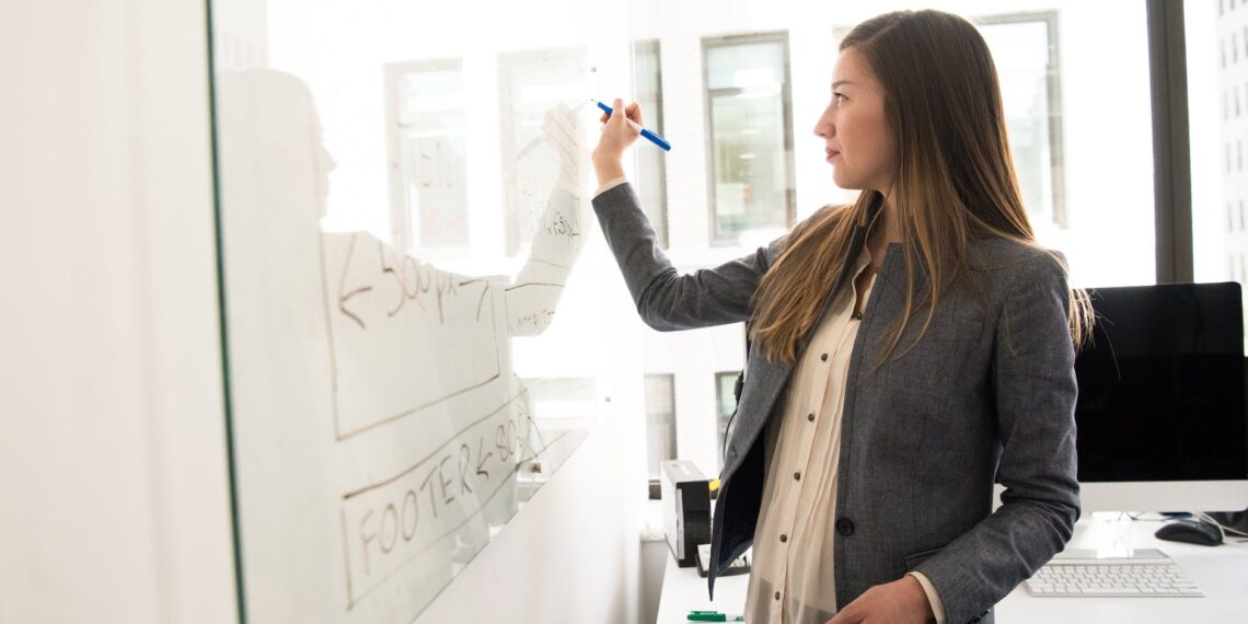 woman wearing gray blazer writing on dry erase board