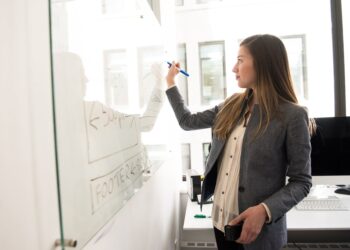 woman wearing gray blazer writing on dry erase board