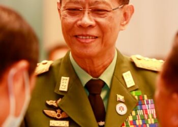 A smiling man in a khaki military uniform with medal ribbons and other insignia on his jacket