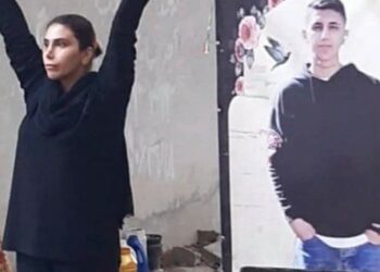 Mahsa Yazdani with her arms raised in front of a large photograph of her son