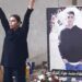Mahsa Yazdani with her arms raised in front of a large photograph of her son