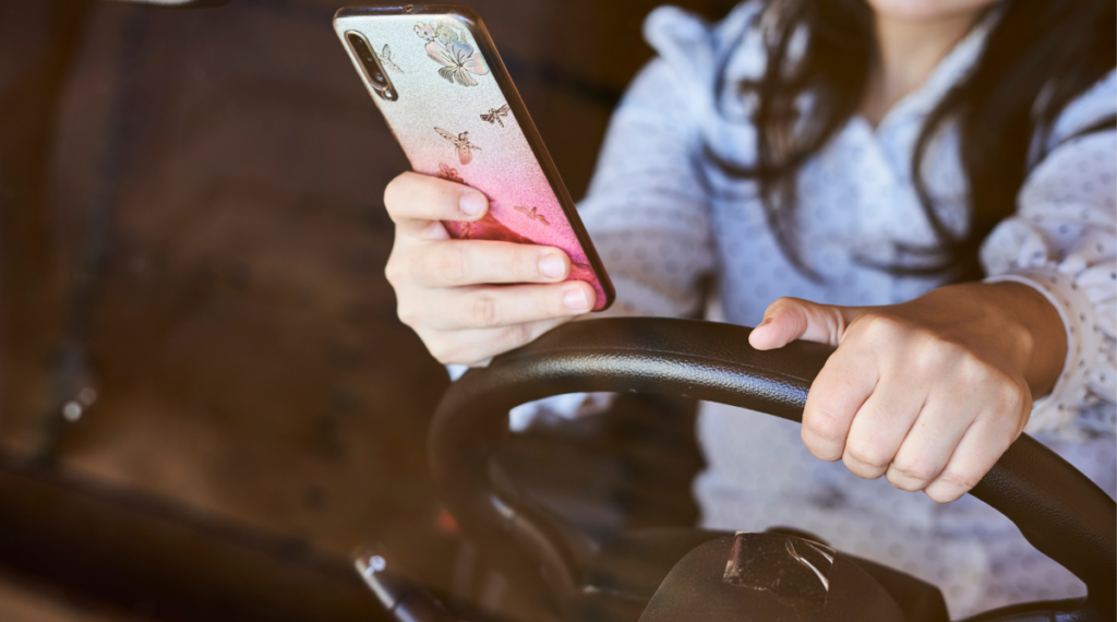 Woman holding her steering wheel in one hand and her phone in the other.