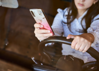 Woman holding her steering wheel in one hand and her phone in the other.