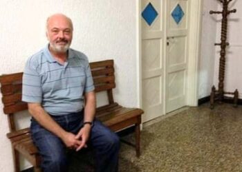 Carlos Luis Malatto sitting on a wooden bench in a house