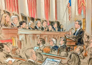 In a full courtroom, the audience looks on as a lawyer stands and discusses his case with all nine justices on the bench.