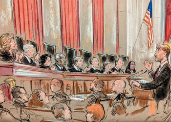All nine justices speaking on the bench to lawyer at lectern with group looking on.