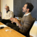 Speaker Nader Andrawos in conversation with moderator Omar Abdel-Ghaffar. They are both sitting at a table in front of a blackboard.